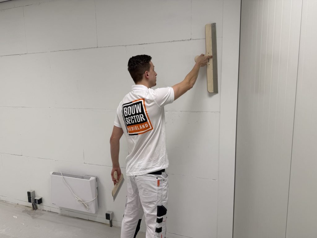 Stukadoor trekt hoog op de muur een nieuwe stuclaag vlak met de spaan