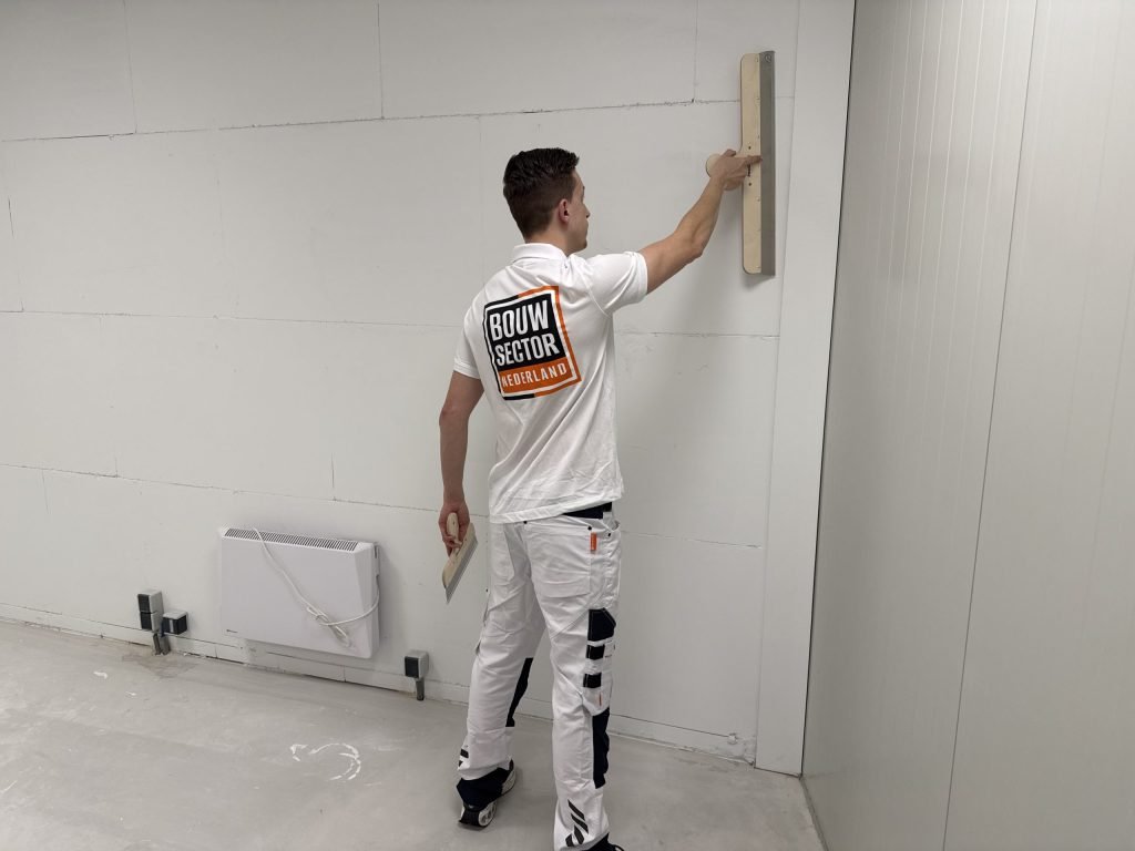 Stukadoor in wit werkpak met spaan en plakspaan voor een grote wand