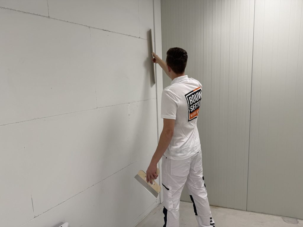 Stukadoor brengt een verse laag pleister aan op een muur naast een roldeur