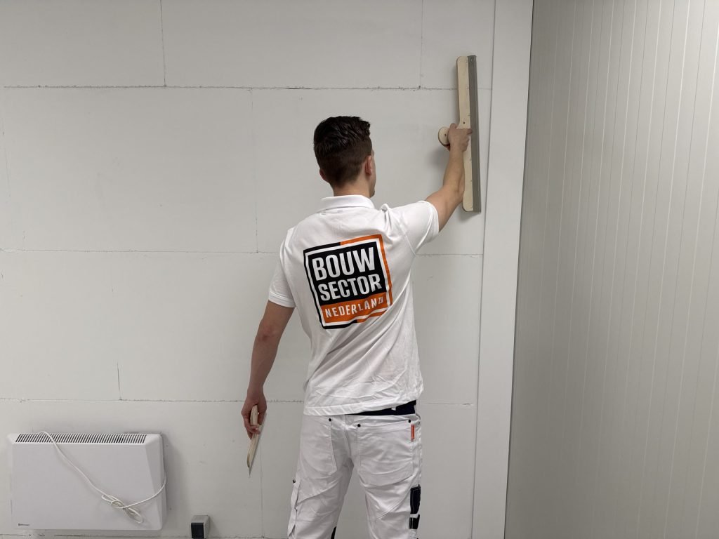 Stukadoor van Bouwsector Nederland zet een lange spaan tegen een gipsplaatwand waarop de naden nog zichtbaar zijn