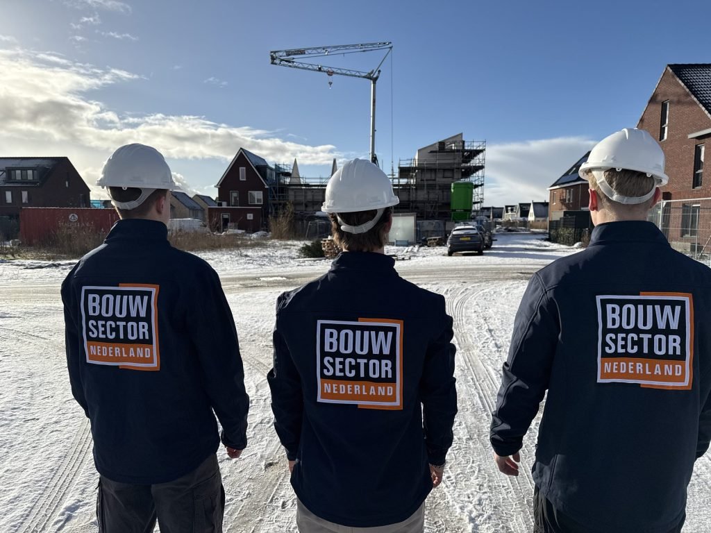 Drie vakmensen van Bouwsector Nederland met witte helm voor een rij nieuwbouwwoningen en een bouwkraan